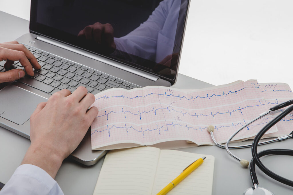 Du siehst ein Blatt Papier mit einer EKG Kurve sowie einen Laptop